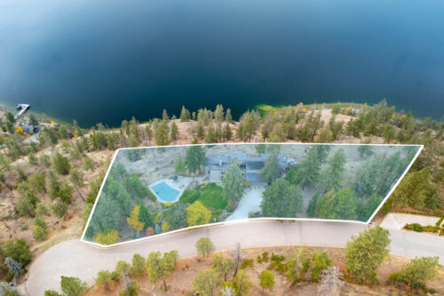 Aerial view of a lakefront lot above Okanagan Lake with its property lines outlined, showing the pool and treed grounds