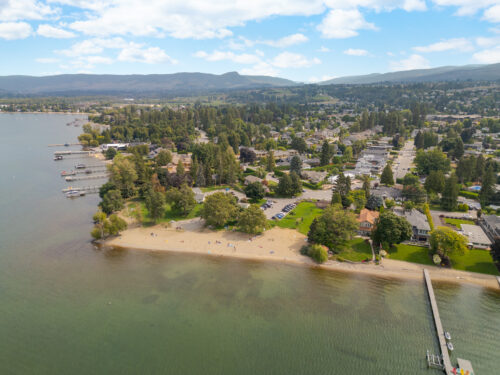 Aerial view of a sandy Okanagan Lake beach with private docks and lakeside homes among mature trees